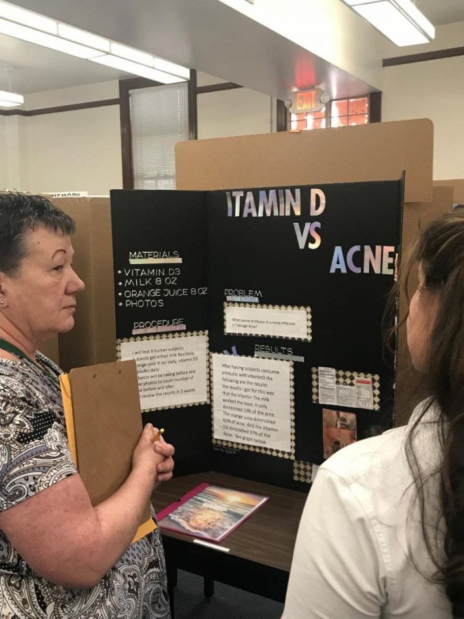 Ms. Ray judging science fair projects. The project being presented is Vitamin D vs. Acne. Photo courtesy of Loretto Academy newsletter. 
