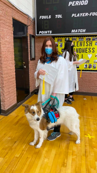 Senior Sydeney Dungan, sporting her graduation gown and bringing a guest of honor. Although she is using a face mask, her smile is evident on her face. 
