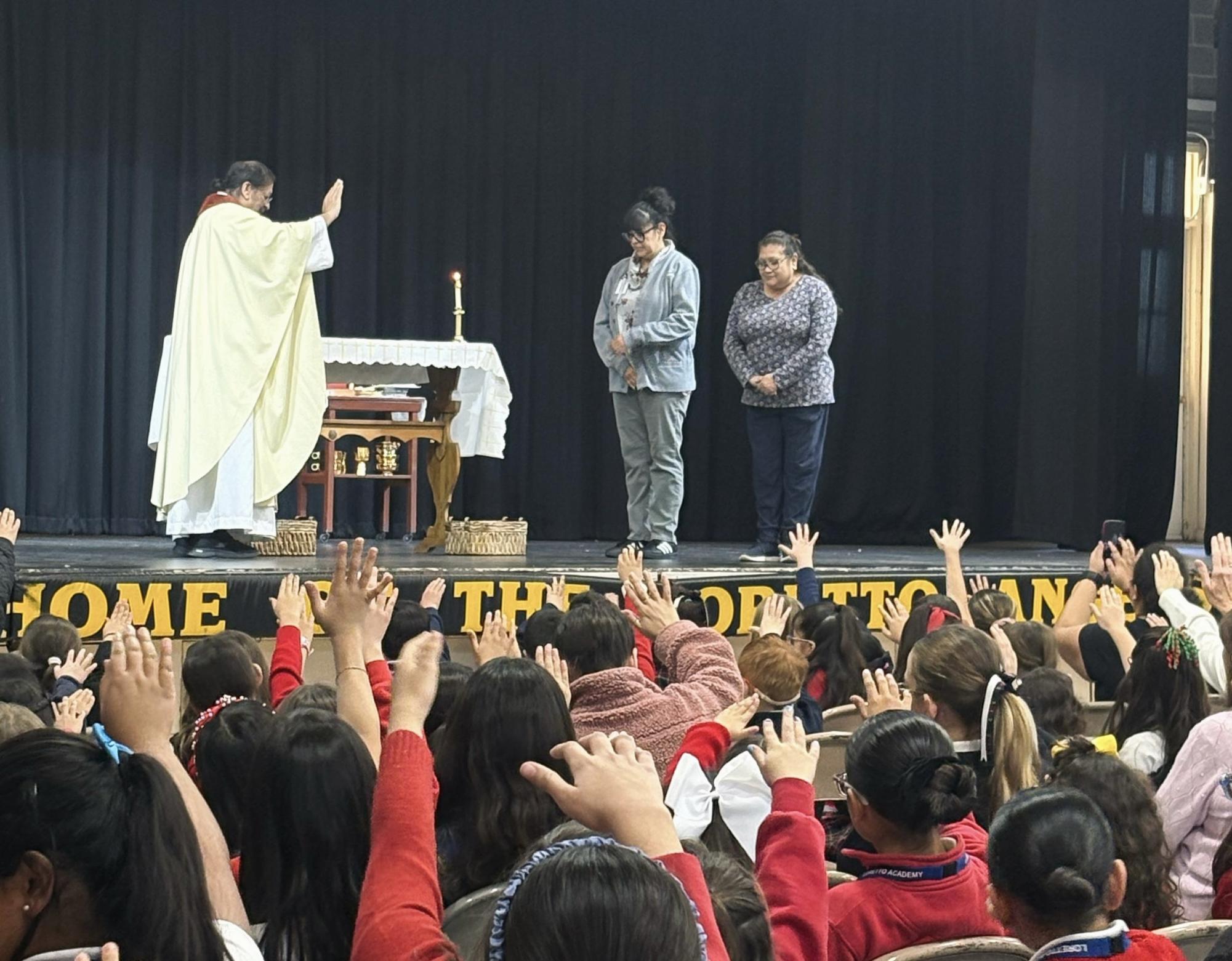 Mrs. Cortez being blessed by Father Ken at the all academy mass on December 8, 2025. Students raised their arms towards the stage as they prayed over the Teacher of the Year 2025. Photo courtesy of Olivia Montelongo. 