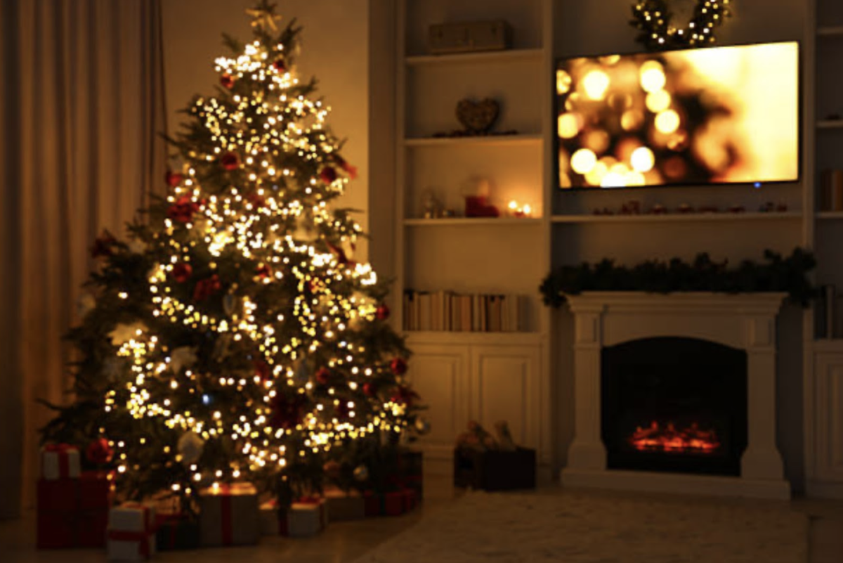 A decorated Christmas tree shines in the room with a TV with a wreath above it. It captures the warm lighting that floods the room. Photo courtesy of flickr.
